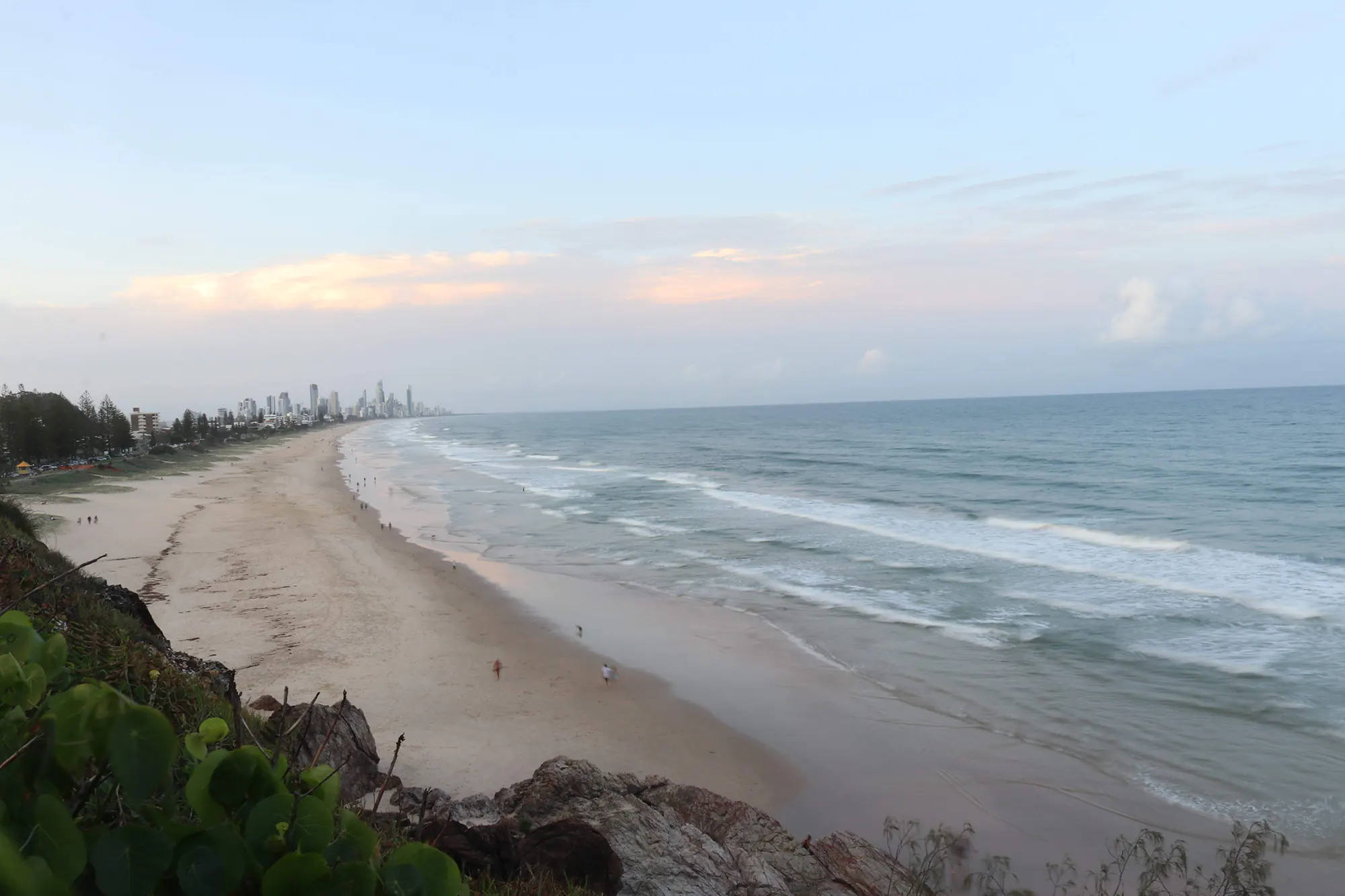 Elevated view of Miami Beach on the Gold Coast, showcasing sandy stretches, rolling waves, coastal greenery, and a distant skyline.